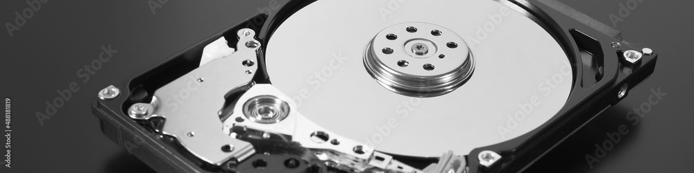 A disassembled open hard disk drive HDD of a computer or laptop lies on a dark surface. IT close up. Black and white banner about computer hardware and equipment. Data storage headline. Macro A disassembled open hard disk drive HDD of a computer or laptop lies on a dark surface. IT close up. Black and white banner about computer hardware and equipment. Data storage headline. Macro