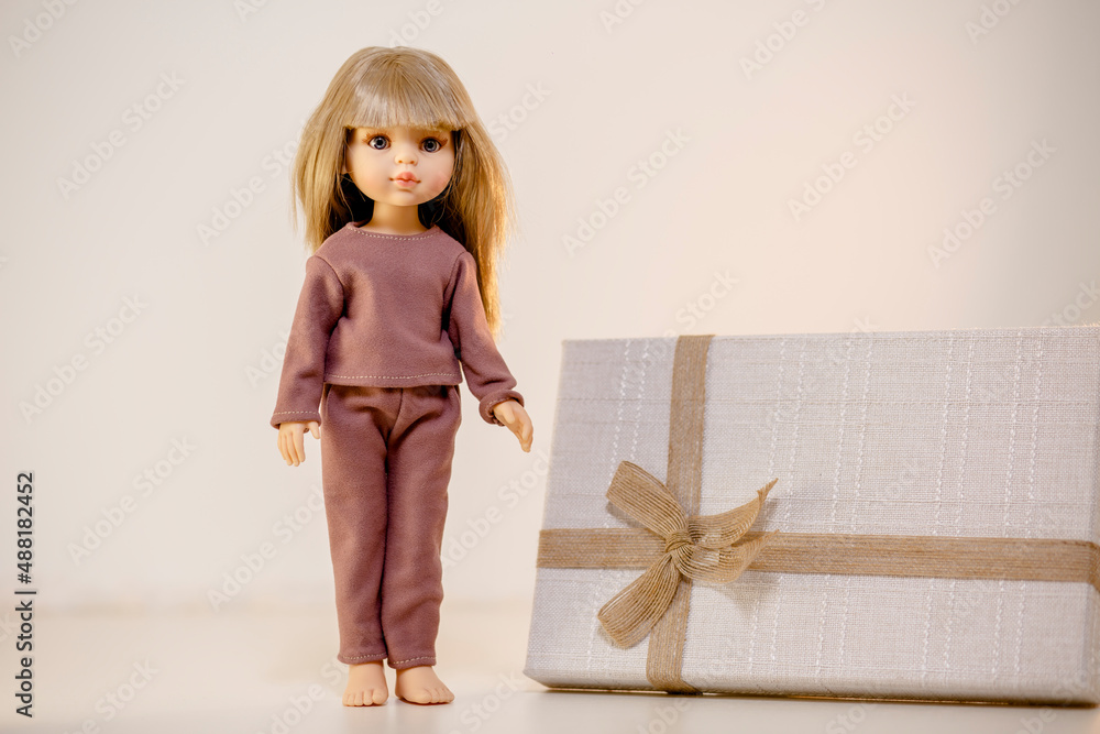 Pretty doll demonstrating her pajamas and standing next to the gift