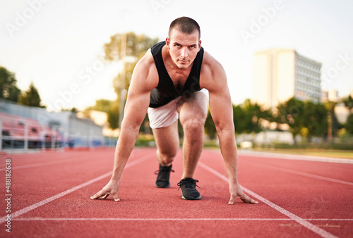 Young millennial determined muscular sportsman starting running on a red running court in a stadium - Athletic motivated runner preparing for running race and looking forward into the distance