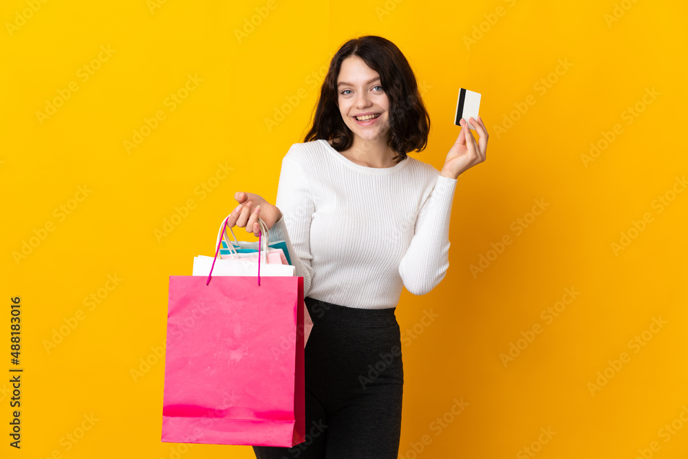 Teenager Ukrainian girl isolated on yellow background holding shopping bags and a credit card Teenager Ukrainian girl isolated on yellow background holding shopping bags and a credit card