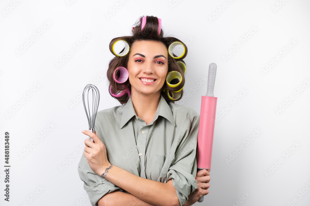 Beautiful housewife. Young cheerful woman with hair curlers, bright make-up, a rolling pin and a whisk in her hands, on a white background. Beautiful housewife. Young cheerful woman with hair curlers, bright make-up, a rolling pin and a whisk in her hands, on a white background.