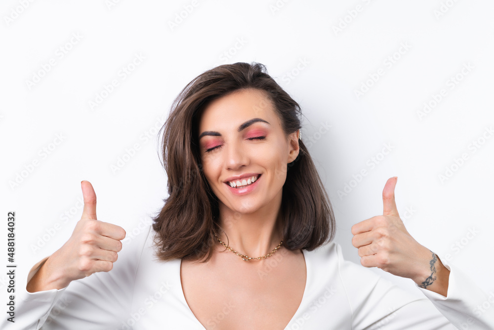 Young woman in a cocktail dress, gold chain and bright spring pink makeup on a white background. Cheerfully smiling showing thumbs up Young woman in a cocktail dress, gold chain and bright spring pink makeup on a white background. Cheerfully smiling showing thumbs up