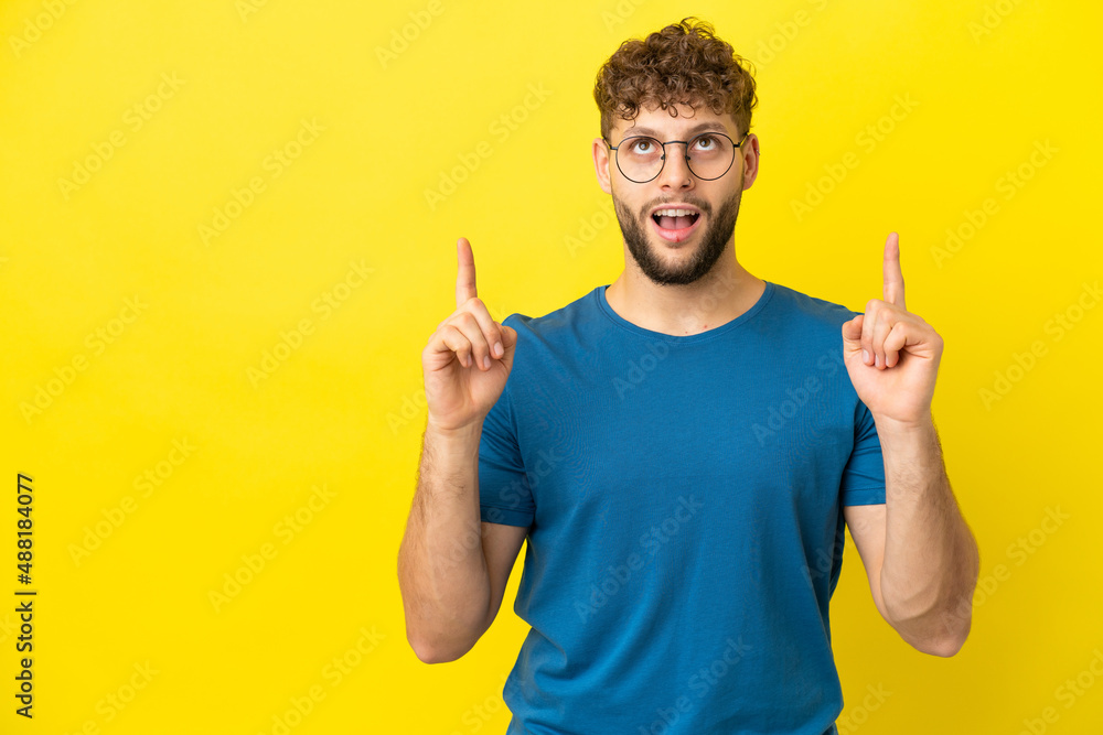 Young handsome caucasian man isolated on yellow background surprised and pointing up Young handsome caucasian man isolated on yellow background surprised and pointing up