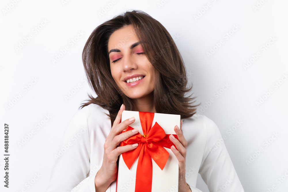 Young woman in a cocktail dress, gold chain, bright spring pink makeup on a white background. Holds a gift box for March 8 and smiles cheerfully. Young woman in a cocktail dress, gold chain, bright spring pink makeup on a white background. Holds a gift box for March 8 and smiles cheerfully.