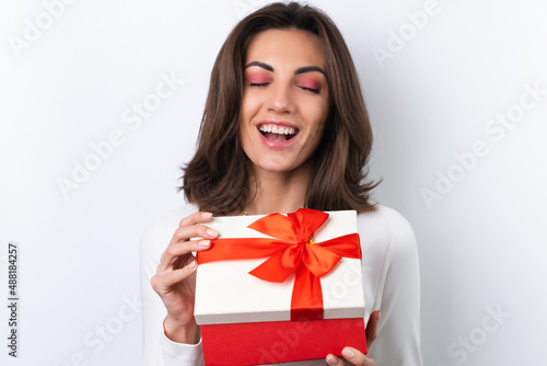 Young woman in a cocktail dress, gold chain, bright spring pink makeup on a white background. Holds a gift box for March 8 and smiles cheerfully.