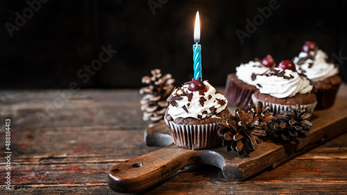 Schwarzwald Geburtstag Hintergrund Grußkarte Postkarte - Schwarzwälder Kirschtorten Cupcakes / Muffins mit Kerze und dekorativen Kieferzapfen, auf altem rustikalem Hozbrett auf Holztisch