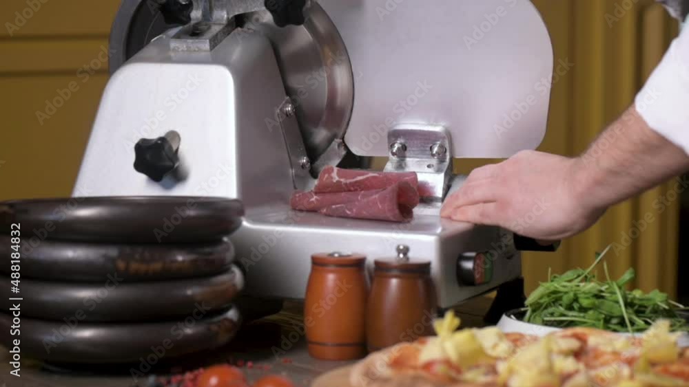 Chef cuts thin slices of ham bacon on cutter for delicious pizza. traditional Italian dish in restaurant or in home kitchen prepared according to classic recipe Chef cuts thin slices of ham bacon on cutter for delicious pizza. traditional Italian dish in restaurant or in home kitchen prepared according to classic recipe