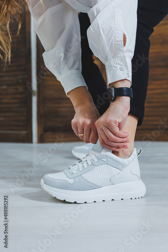Beautiful women s shoes with legs  leather white sneakers  in the interior of a room or office  shoes for a woman  black trousers and white sneakers  casual and modern style  modern and trendy