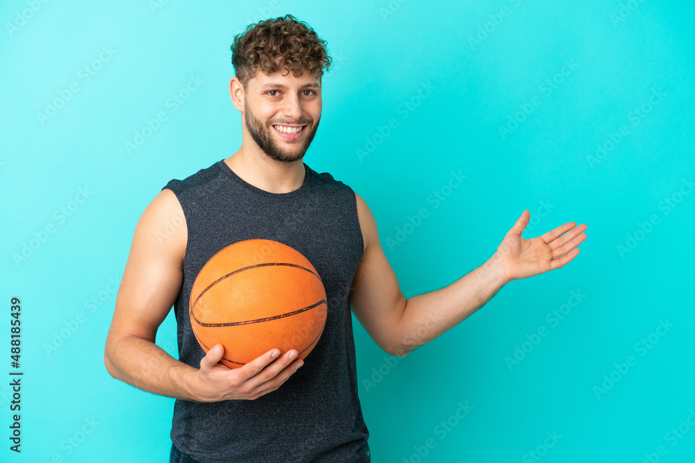 Handsome young man playing basketball isolated on blue background extending hands to the side for inviting to come