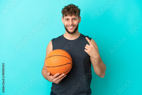Handsome young man playing basketball isolated on blue background giving a thumbs up gesture