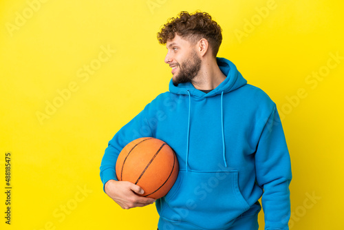 Young handsome caucasian man isolated on yellow background playing basketball