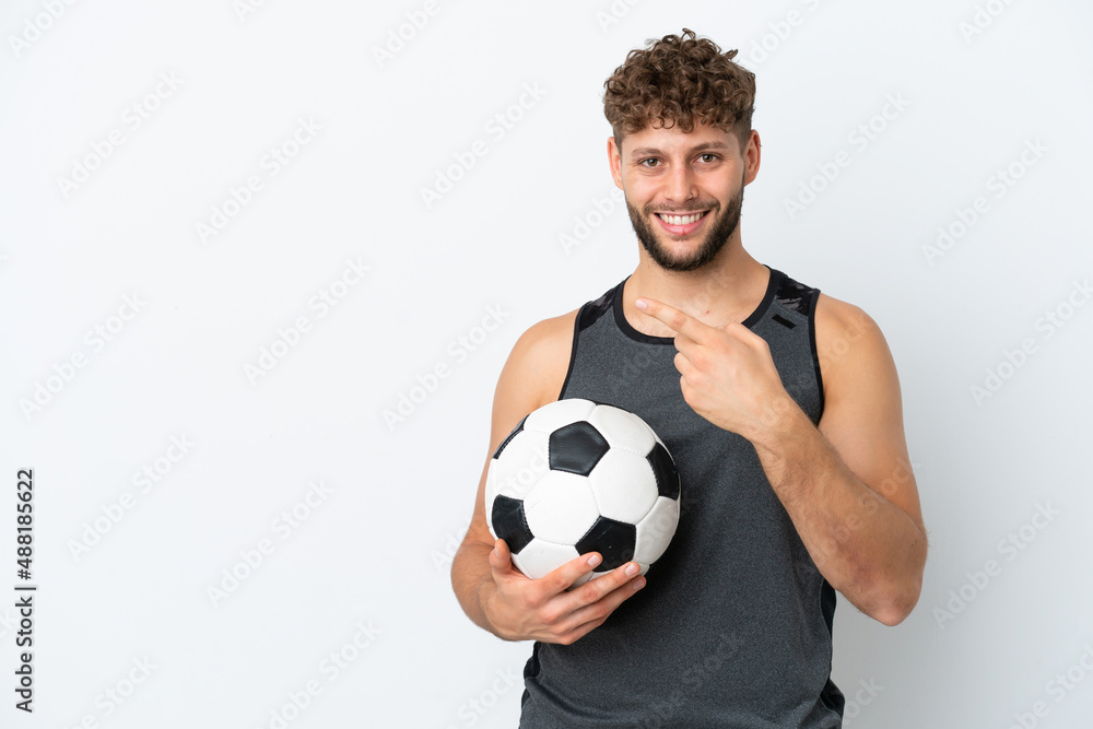 Young handsome caucasian man isolated on white background with soccer ball and pointing to the lateral