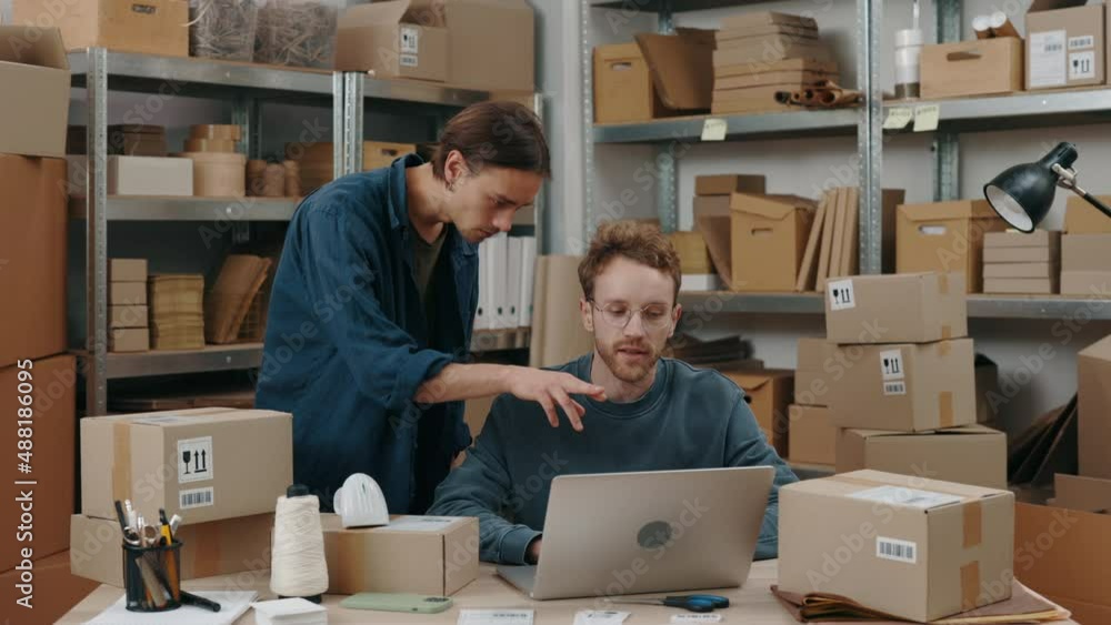 Look there. Brunette man looking at the laptop screen and discussing some details with his caucasian male colleague while working together at the warehouse. Small business concept. Look there. Brunette man looking at the laptop screen and discussing some details with his caucasian male colleague while working together at the warehouse. Small business concept.