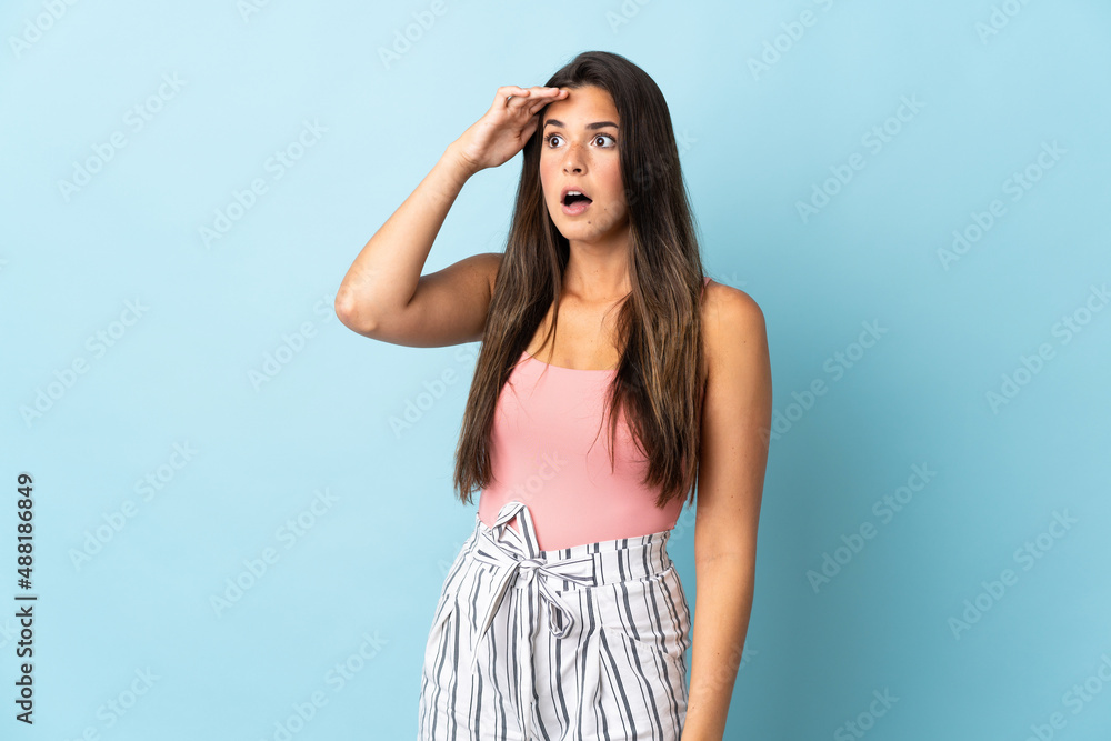 Young brazilian woman isolated on blue background with surprise expression while looking side Young brazilian woman isolated on blue background with surprise expression while looking side