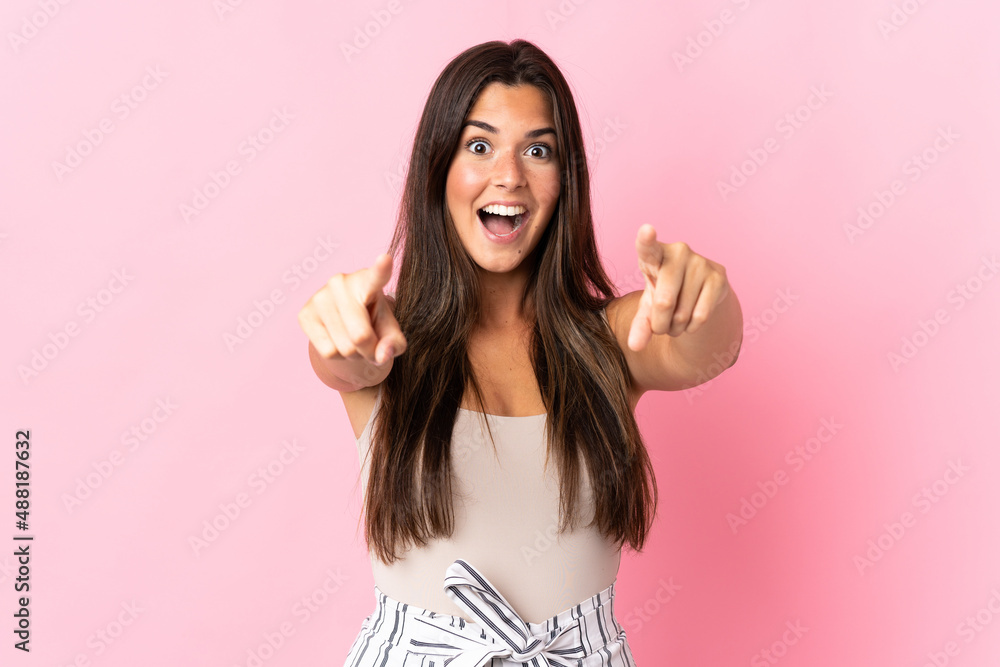 Young brazilian woman isolated on pink background surprised and pointing front Young brazilian woman isolated on pink background surprised and pointing front