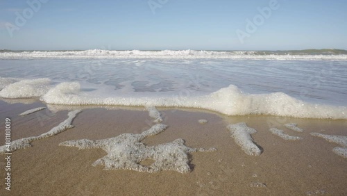 POV of gentle foamy waves moving up towards a pristine beach on the North Sea, Belgian coast photo