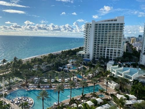 Miami Beach scene of fancy pool area at a hotel with ocean and clouds in background
