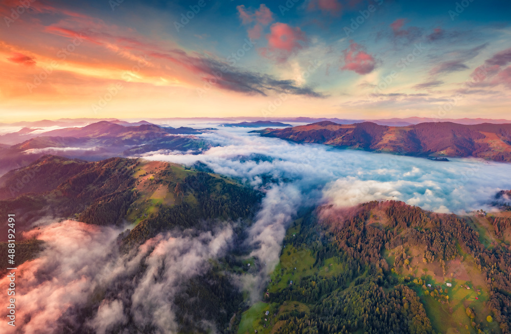 Unbelievable colors sunrise on Carpathian mountains. Fog spreads on the valley of Snidavka village, Ukraine. Spectacular landscape of mountain hills glowing by sunlight.