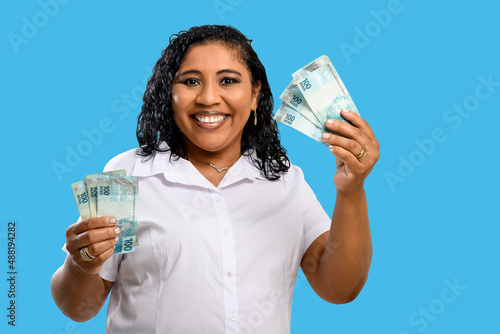woman holds money, smiling brunette woman holds 100 reais banknotes in hands, brazilian money, blue background