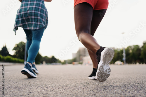 Back view of friends legs in sportswear running in the city. Multiethnic women having a fitness workout.