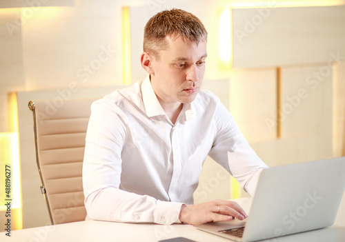 Serious attentive focused businessman sits in the office at a large table in front of a laptop and works online, video chat, communication on working moments on the Internet, work from the office