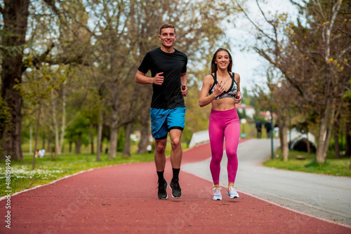Woman and man jogging on red path in the city park together