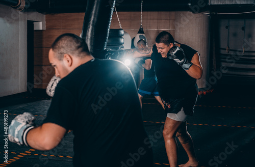 Young Caucasian boxer training alone with punching bag in health club