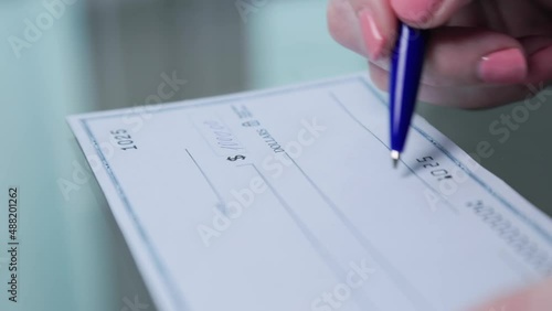 business woman hand signs and filling bank check for one thousand 1000 dollars