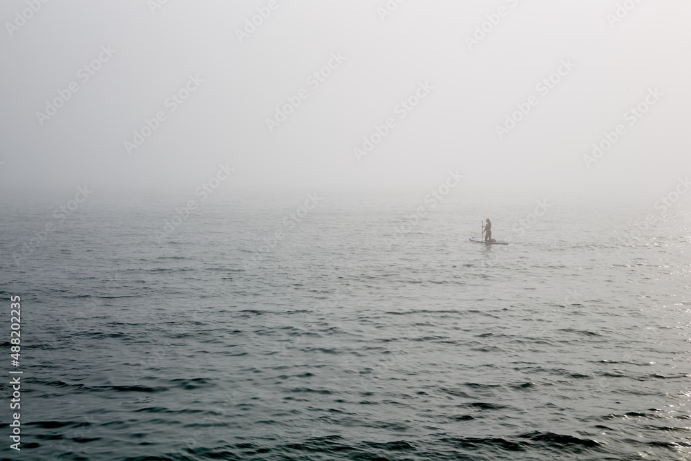 Fototapeta premium A man surfing in the fog on the sea in the distance.