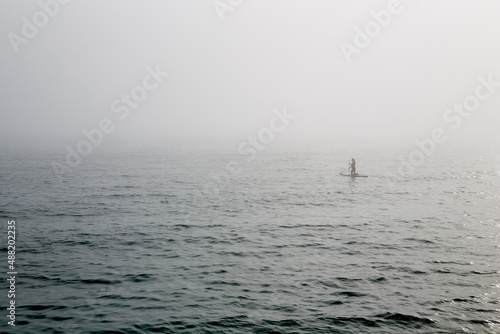 A man surfing in the fog on the sea in the distance.