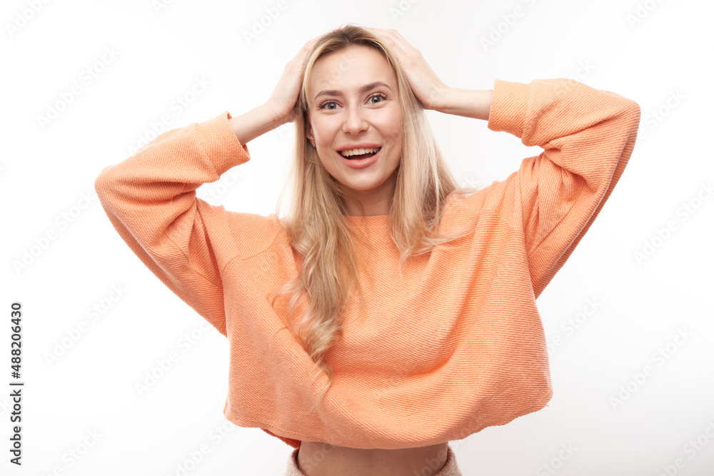 Shocked blond girl looks surprised holding head with hands on white studio background with copy space Shocked blond girl looks surprised holding head with hands on white studio background with copy space