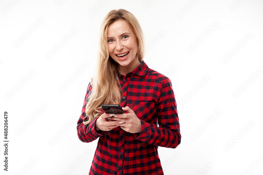 Beautiful blonde girl in casual looks at the smartphone screen and smiles isolated on white studio background Beautiful blonde girl in casual looks at the smartphone screen and smiles isolated on white studio background