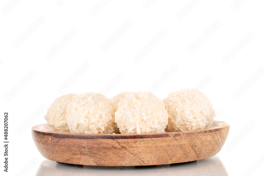A few sweet coconut candies on a wooden saucer, macro, isolated on a white background. A few sweet coconut candies on a wooden saucer, macro, isolated on a white background.