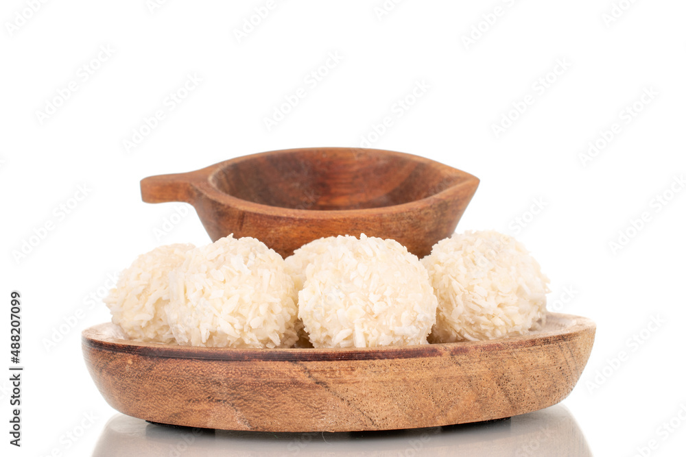 A few sweet coconut candies on a wooden saucer with a wooden cup, macro, isolated on a white background.