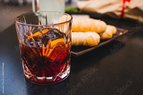 glass of dark vermouth drink with slice of orange on a bar table outdoors, a popular aperitif, during a summer day with snacks and appetizers photo