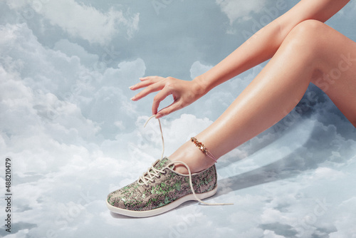 Woman leg with anklet in stylish lumina sage sneaker isolated on blue cloud sky background, space for text photo