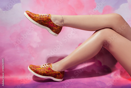 Woman legs with anklet in stylish golden red sneakers isolated on  pink cloud sky background, space for text photo