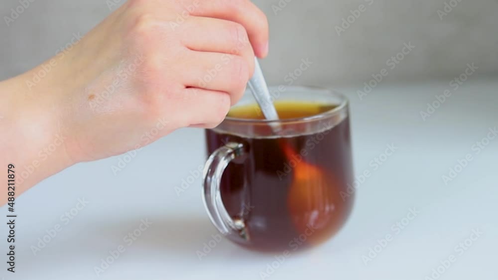 A glass mug with black coffee is on the table. A woman's hand is stirring coffee with a spoon. An invigorating breakfast. A glass mug with black coffee is on the table. A woman's hand is stirring coffee with a spoon. An invigorating breakfast.