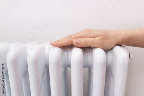 Woman warms up hands over heater. Concept of the need for good central heating. Girl warms the frozen hands above a hot of the radiator, close up. 