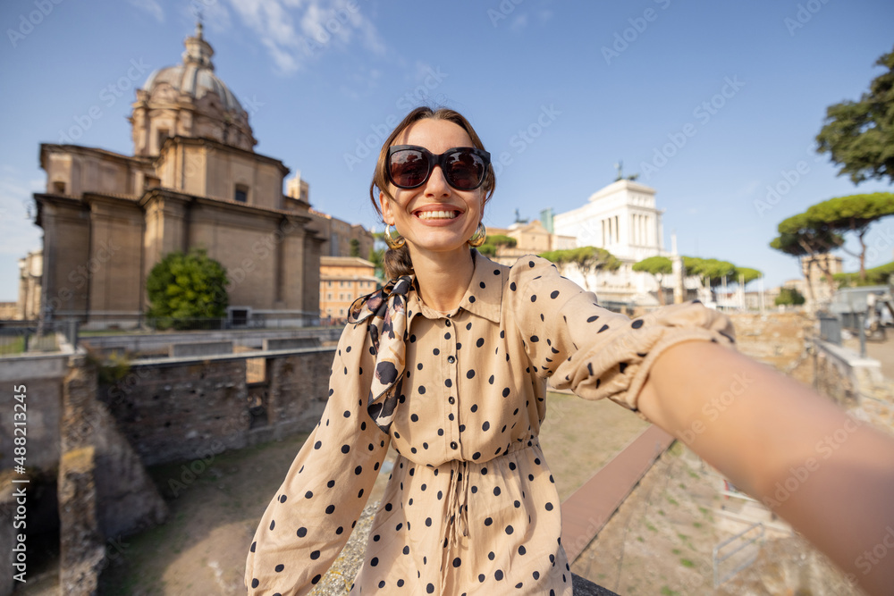 Woman taking selfie photo in front of the Roman Forum, ruins at the center of Rome. Concept traveling famous landmarks in Italy. Caucasian woman wearing dress and shawl in hair