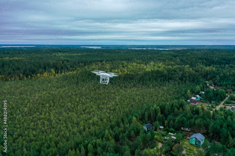 Hovering drone in the white sky over the forest, blue sky with w