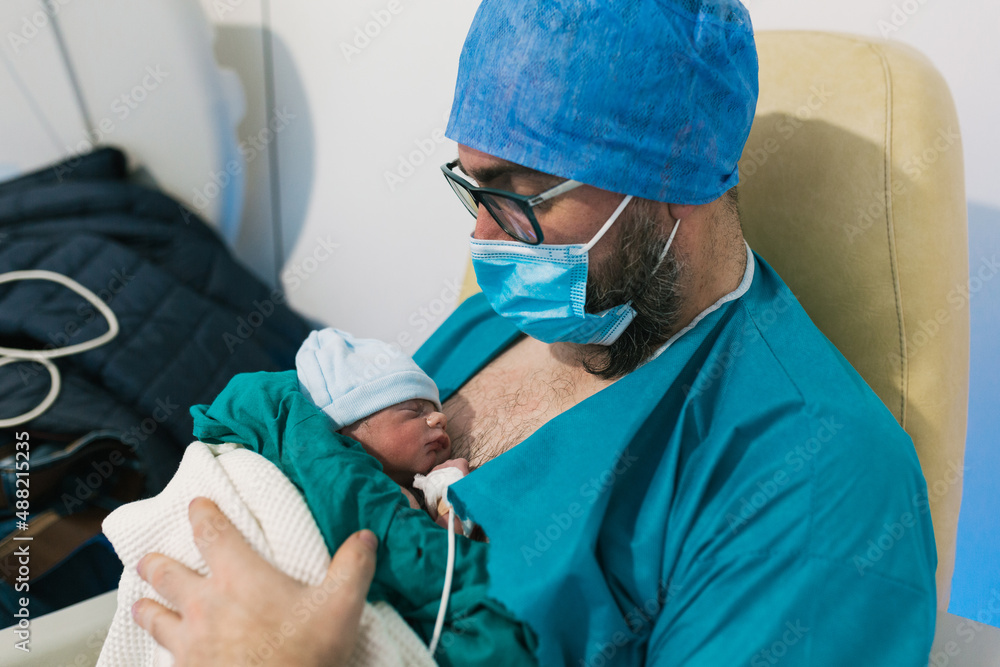 An adult man siting and holding his newborn baby in hospital An adult man siting and holding his newborn baby in hospital