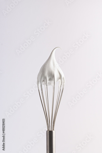 Meringue. Confectionery whipped cream on a whisk. Close-up of a shiny metal whisk with a tip of meringue, emphasizing texture and quality on a white background. photo