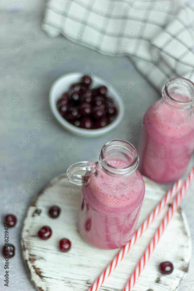 A bottle of cherry smoothies on a white background, cherries in bulk and in a plate. Morning summer breakfast A bottle of cherry smoothies on a white background, cherries in bulk and in a plate. Morning summer breakfast