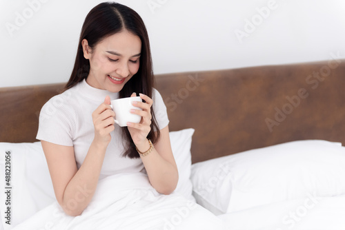 Beautiful asian woman Drinking coffee And happy smile On the bed in the white bedroom