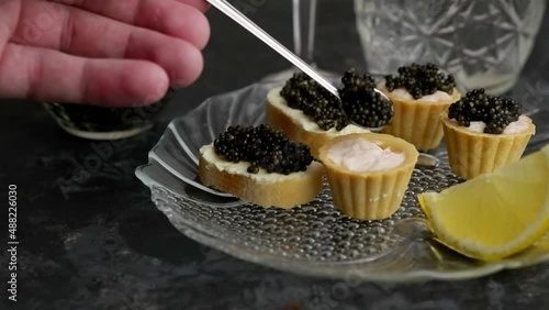 The process of putting black caviar into a tartlet with cream with a spoon.