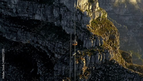 Aerial shot tracking forward and tilting down to follow the movement of a cable car coming down from Table Mountain Cape Town.