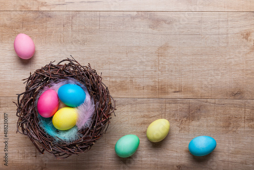 Nest with colorful Easter eggs and feathers in pastel colors on a wooden background. Minimalist easter concept with copy space, top view. Background, postcard with Easter decorations.