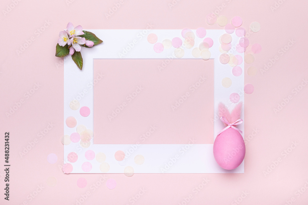 Creative easter concept with pink egg with fluffy bunny ears and apple bloom on pink background with copy space. White frame with pastel colored confetti and place for text, top view.