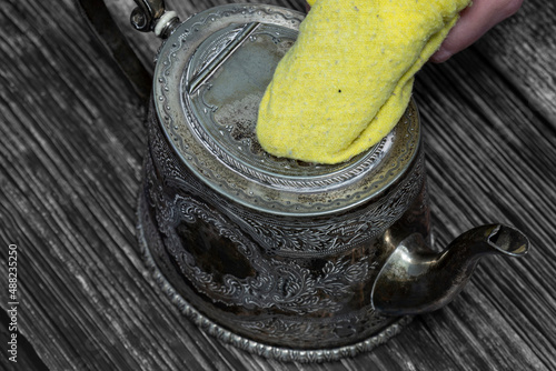 Cleaning antique tarnished silver teapot with a yellow duster. On a wood background